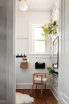 a white room with a chair, mirror and plant on the window sill in it