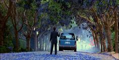 a man standing next to a blue car on a road with trees in the background