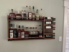 an assortment of liquor bottles are displayed on a wooden shelf in a room with white walls