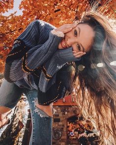 a woman posing for a selfie with her hair blowing in the wind and wearing ripped jeans