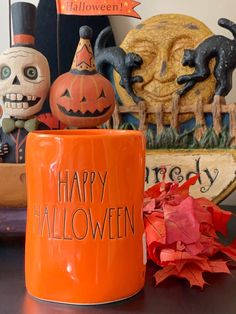 an orange coffee mug sitting on top of a table with halloween decorations and pumpkins