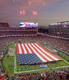 an american flag is displayed in the middle of a football stadium as fireworks go off