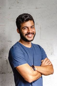 a man standing with his arms crossed in front of a white wall and smiling at the camera