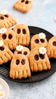 small cookies decorated with jelly and flowers are on a black plate next to white daisies