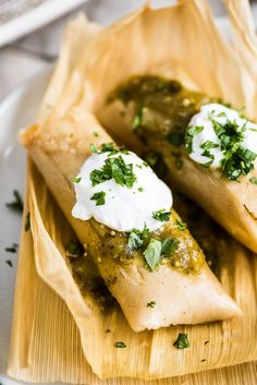 two burritos on a plate with sour cream and cilantro garnishes