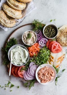 a platter filled with different types of vegetables and dips next to bagels