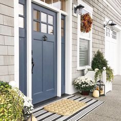 a blue front door with white flowers and potted plants next to it on a black and white striped rug