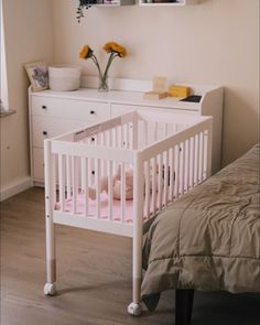 a white crib in a bedroom next to a bed and dresser with flowers on it