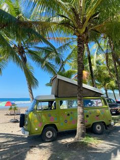 a green van parked on top of a sandy beach next to palm trees and the ocean