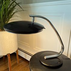 a black table lamp sitting on top of a wooden floor next to a potted plant