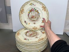 a stack of plates sitting on top of a table next to a person's hand