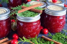 several jars filled with cranberry sauce surrounded by cinnamon sticks and fresh greenery