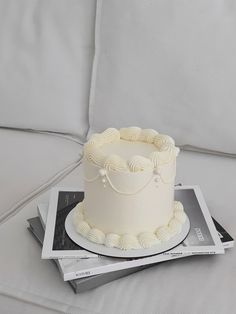 a white cake sitting on top of a table next to a stack of magazine's