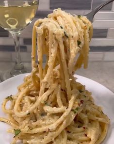 a white plate topped with pasta next to a glass of wine