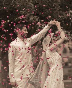 a man and woman standing next to each other under a tree with petals in the air