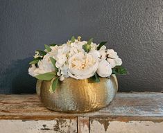 a gold vase filled with white flowers on top of a wooden table