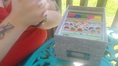 a woman sitting in front of a box filled with lots of different colored stickers