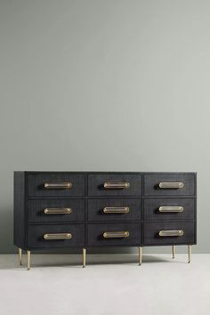 a black and gold dresser with brass handles on it, against a gray wall in an empty room