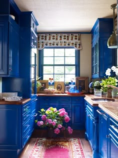 a kitchen with blue cabinets and pink flowers on the counter top in front of a window