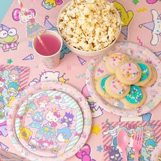 a table topped with lots of pink and blue plates covered in food next to a bowl of popcorn