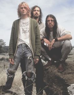 two men sitting on top of a pile of dirt next to another man with long hair