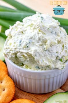 a white bowl filled with cream cheese surrounded by crackers and cucumbers