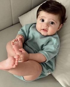 a baby sitting on top of a couch with his feet up and looking at the camera