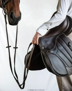 a man is holding the bridle of a horse's saddle while standing next to it