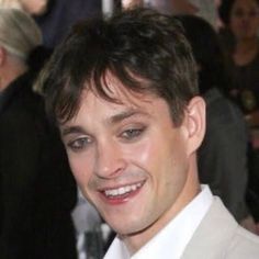 a man in a suit and tie smiling at the camera with other people behind him