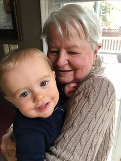 an older woman is holding a baby in her arms and smiling at the camera,