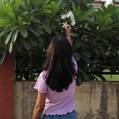 a woman reaching up to a plant with white flowers