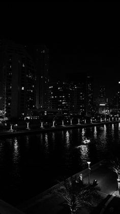 black and white photograph of city lights along the riverbank at night with buildings in the background