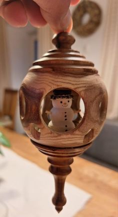 a hand holding a wooden object with a snowman inside