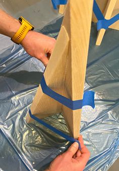 two hands are working on an object that is being made out of plywood and blue tape