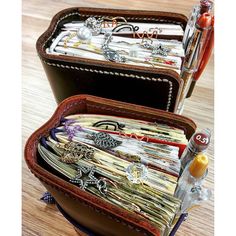 two brown leather wallets filled with lots of papers and jewelry sitting on top of a wooden table