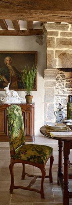 a dining room table with chairs and a painting on the wall behind it, in front of a fireplace