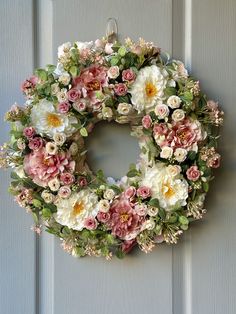 a floral wreath hanging on the front door with pink and white flowers around it,