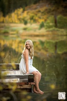 a beautiful blonde woman sitting on top of a wooden bench next to a body of water