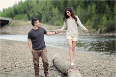 a man and woman holding hands while standing on a log in front of a river