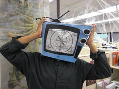 a man with a tv on his head in an office cubicle, holding up the television