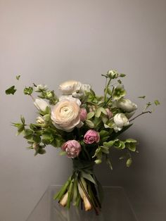 a vase filled with white and pink flowers on top of a glass table next to a gray wall