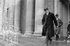 an old black and white photo of two men walking in front of a building with columns