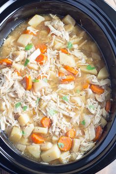 a crock pot filled with chicken, potatoes and carrots on top of a wooden table