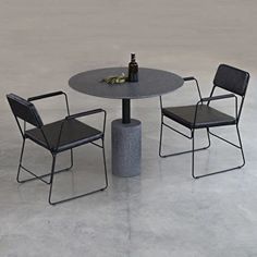 a table with two chairs and a wine bottle on it, in front of a concrete wall