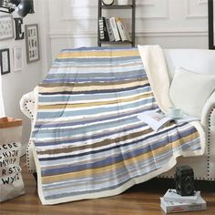 a living room with a white couch and striped blanket on top of the sofa, next to a bookshelf