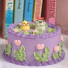 there is a cake decorated with purple icing and flowers on the table next to books