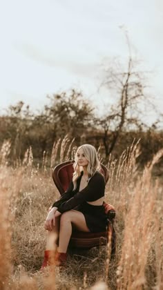 a woman sitting on top of a brown chair in a field with tall dry grass