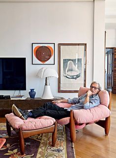 a man sitting in a pink chair with his feet up on the ottoman while talking on a cell phone