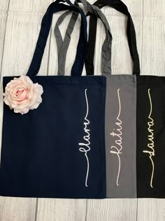 two black and gray shopping bags with pink flower on the front, one in grey and one in white