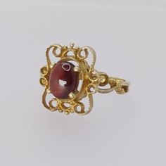 Indulge in the timeless beauty of the Art Nouveau era with this exquisite vintage ring. Meticulously crafted from hallmarked 9ct yellow gold, this ring features a lustrous Cabochon garnet gemstone that exudes vintage charm, making it a perfect addition to any outfit. Key Features: - Metal: Hallmarked 9ct Yellow Gold - Gemstone: Cabochon Garnet - Garnet Dimensions: Approximately 7.8mm by 6.4mm - Ring Size: UK Size M/N - Weight: 2.8 grams - Head Dimensions: Approximately 15.1mm by 13.2mm This ring Vintage Garnet Birthstone Ring In Yellow Gold, Vintage Yellow Gold Garnet Birthstone Ring, Yellow Gold Garnet Ring With Polished Finish, Red Cabochon Ruby Ring In 14k Gold, 14k Gold Red Cabochon Ruby Ring, Vintage Gold Garnet Birthstone Ring, Ornate Gold Ruby Ring, 14k Gold Cabochon Red Ring, 14k Gold Red Cabochon Ring